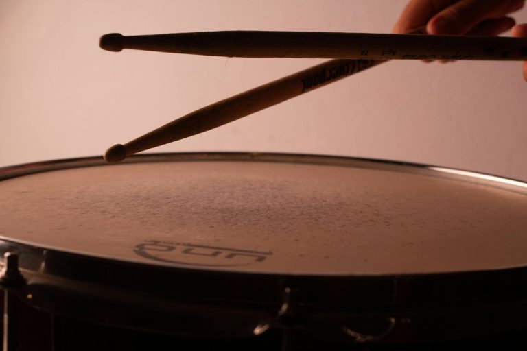 Crop musician playing drum using wooden drumsticks